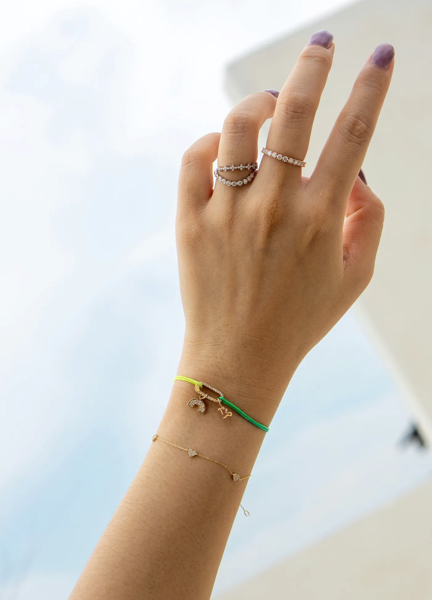 Hand mit feinen Armbändern und kleinen Charms vor hellem Himmel