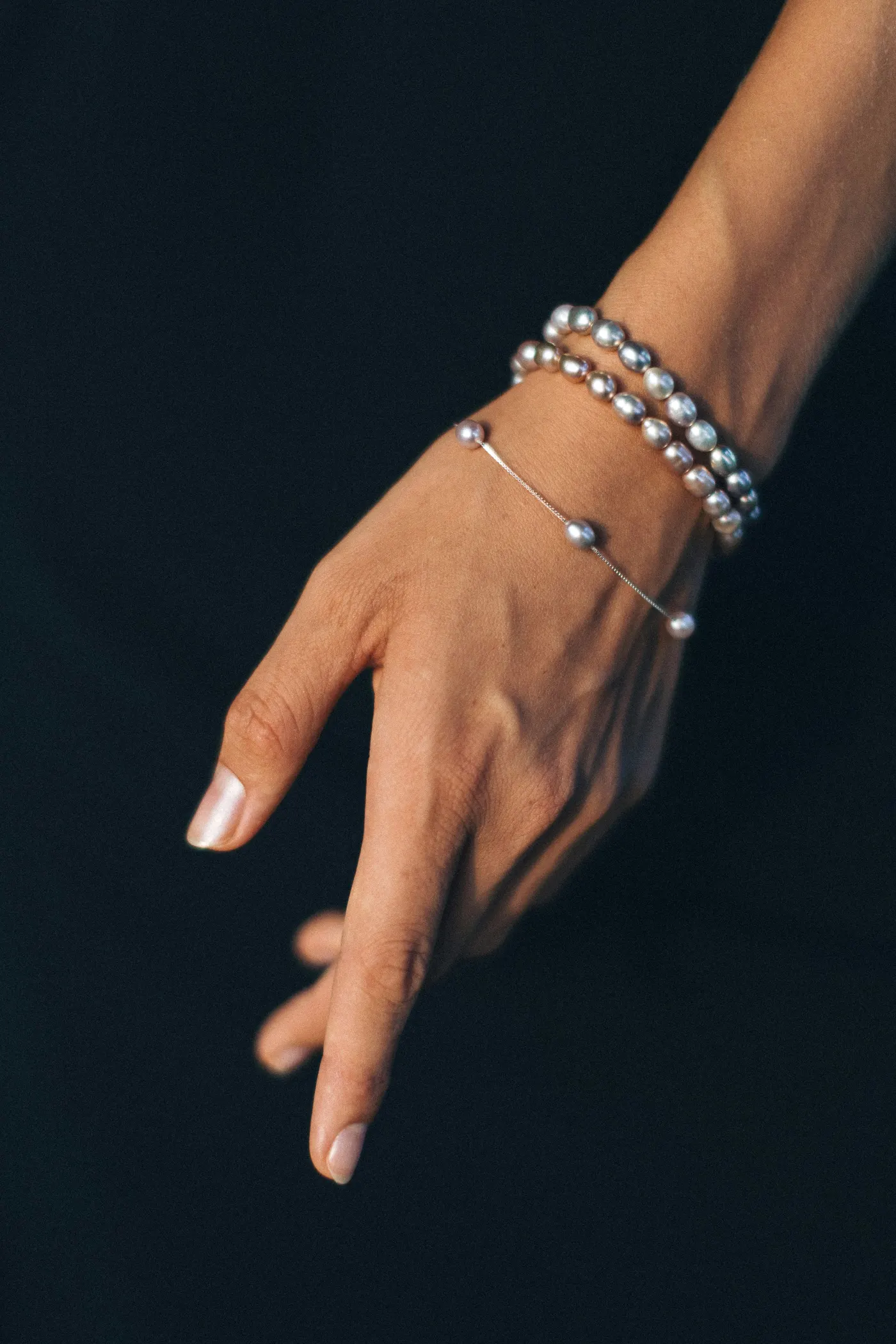 Silbernes Armband mit Perlen an einer Hand vor dunklem Hintergrund